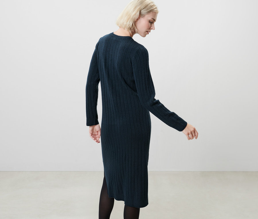Blondynka pozuje w granatowej sukience z prążkowanej dzianiny.