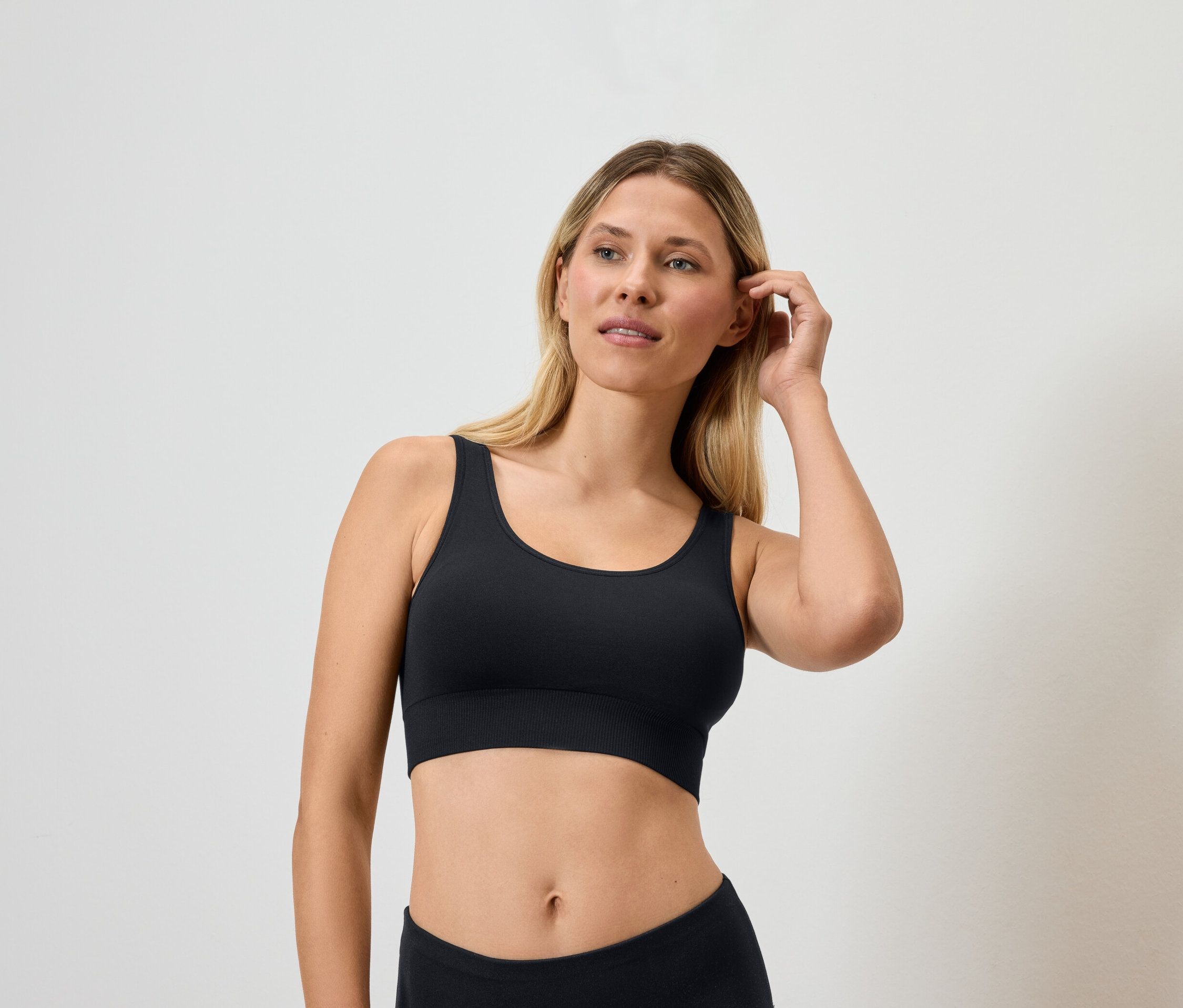 Blondynka w czarnym biustonoszu sportowym dotyka włosów.
