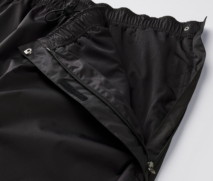 Zbliżenie na czarne spodnie przeciwdeszczowe high-tech z rozpiętym zamkiem błyskawicznym i widoczną podszewką z siateczki.