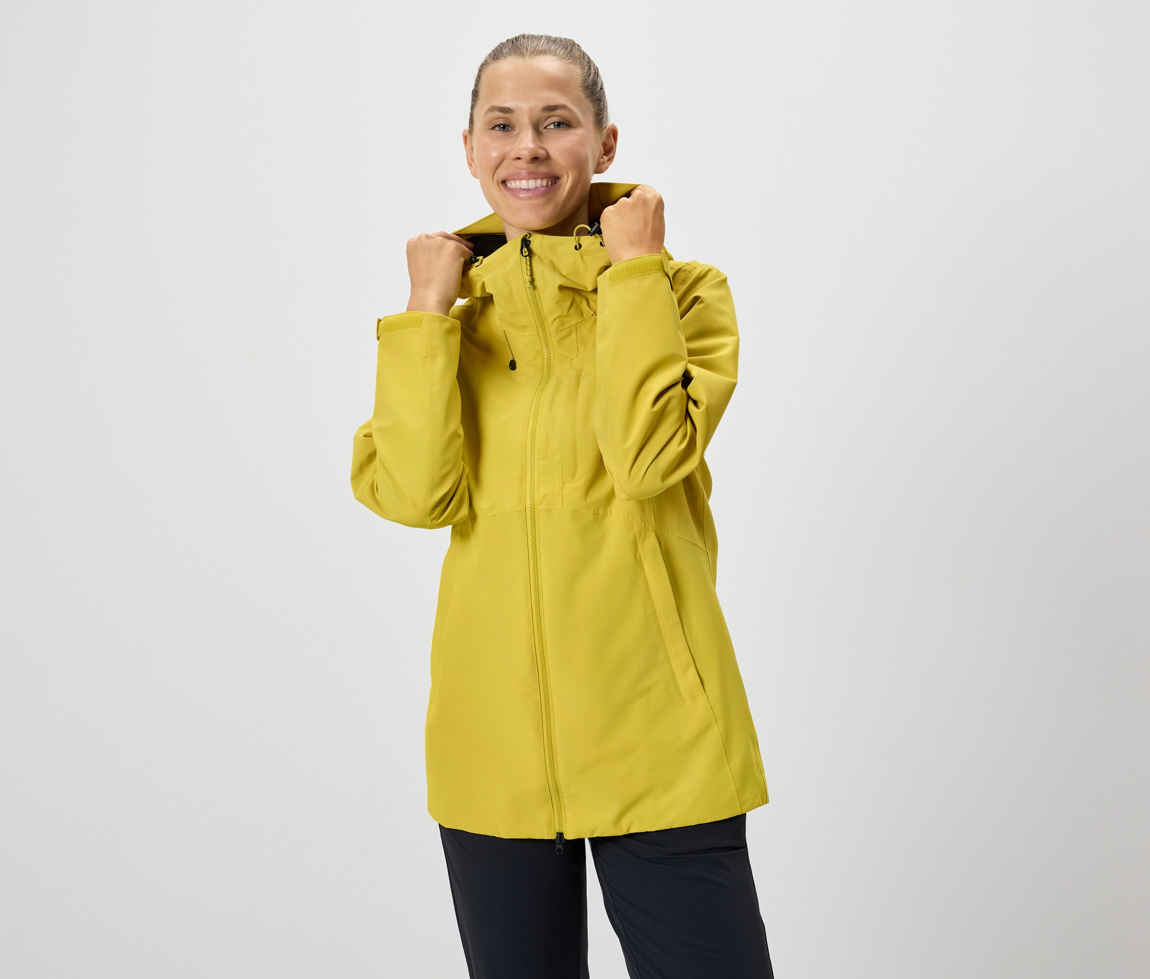 Kobieta poprawia kaptur żółtej kurtki na zamek błyskawiczny.