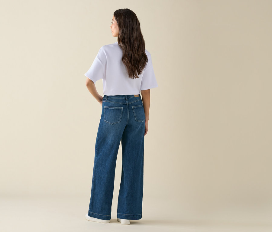 Kobieta pozuje w szerokich dżinsach i białym T-shircie.