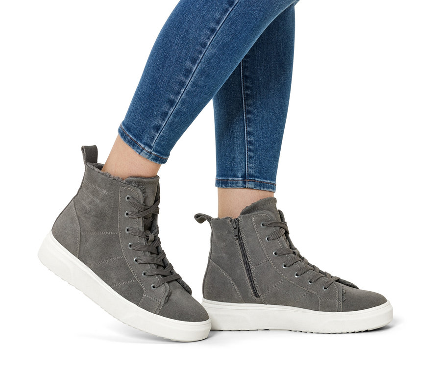 Nogi w niebieskich dżinsach i szarych zamszowych butach na białych podeszwach.