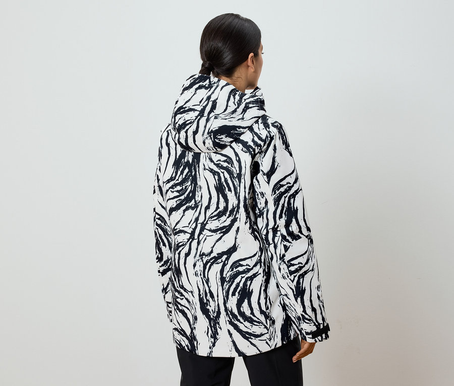 Widok z tyłu kobiety w czarno-białej kurtce we wzory z kapturem i kucykiem.