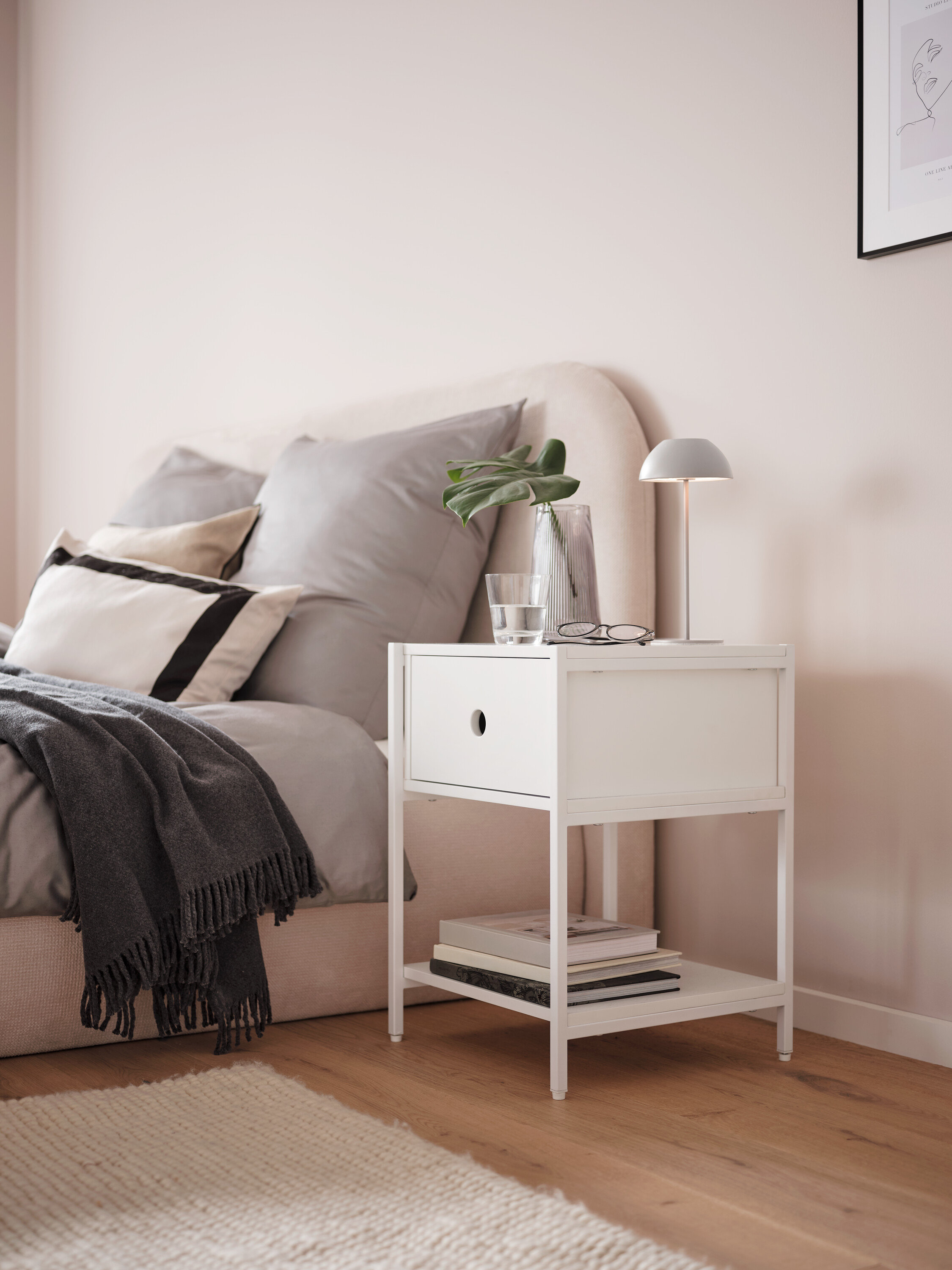 Szara akumulatorowa lampa stołowa LED na białym stoliku nocnym obok łóżka.