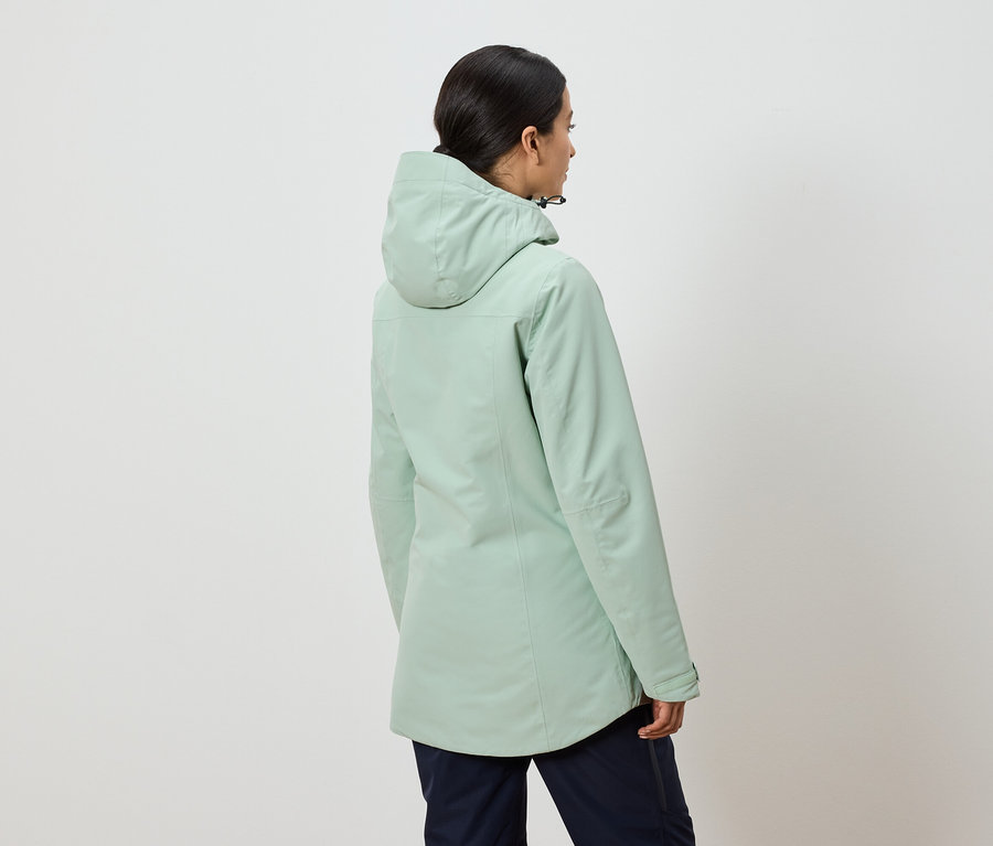 Widok z tyłu kobiety w miętowo-zielonej kurtce z kapturem i granatowych spodniach.