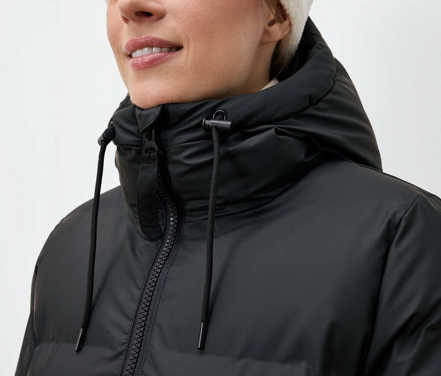 Kobieta ma na sobie czarną kurtkę puchową i białą czapkę.