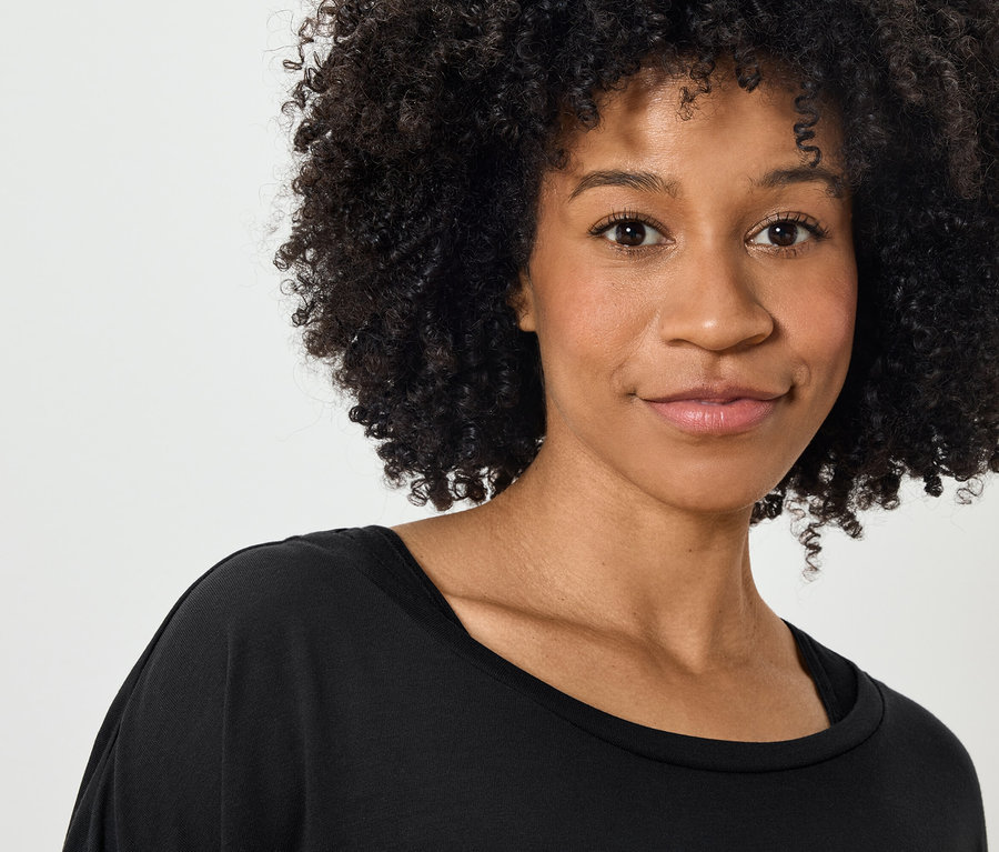 Portret uśmiechniętej kobiety z kręconymi włosami w czarnej koszulce.