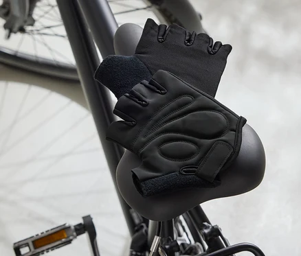 Dwie czarne rękawice rowerowe leżą na czarnym siodełku rowerowym.