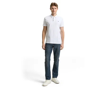 Mężczyzna w białej koszulce polo i dżinsach Tom Tailor TT MARVIN STRAIGHT ze stretchem, Mid Stone Blue Grey Denim i białych butach.