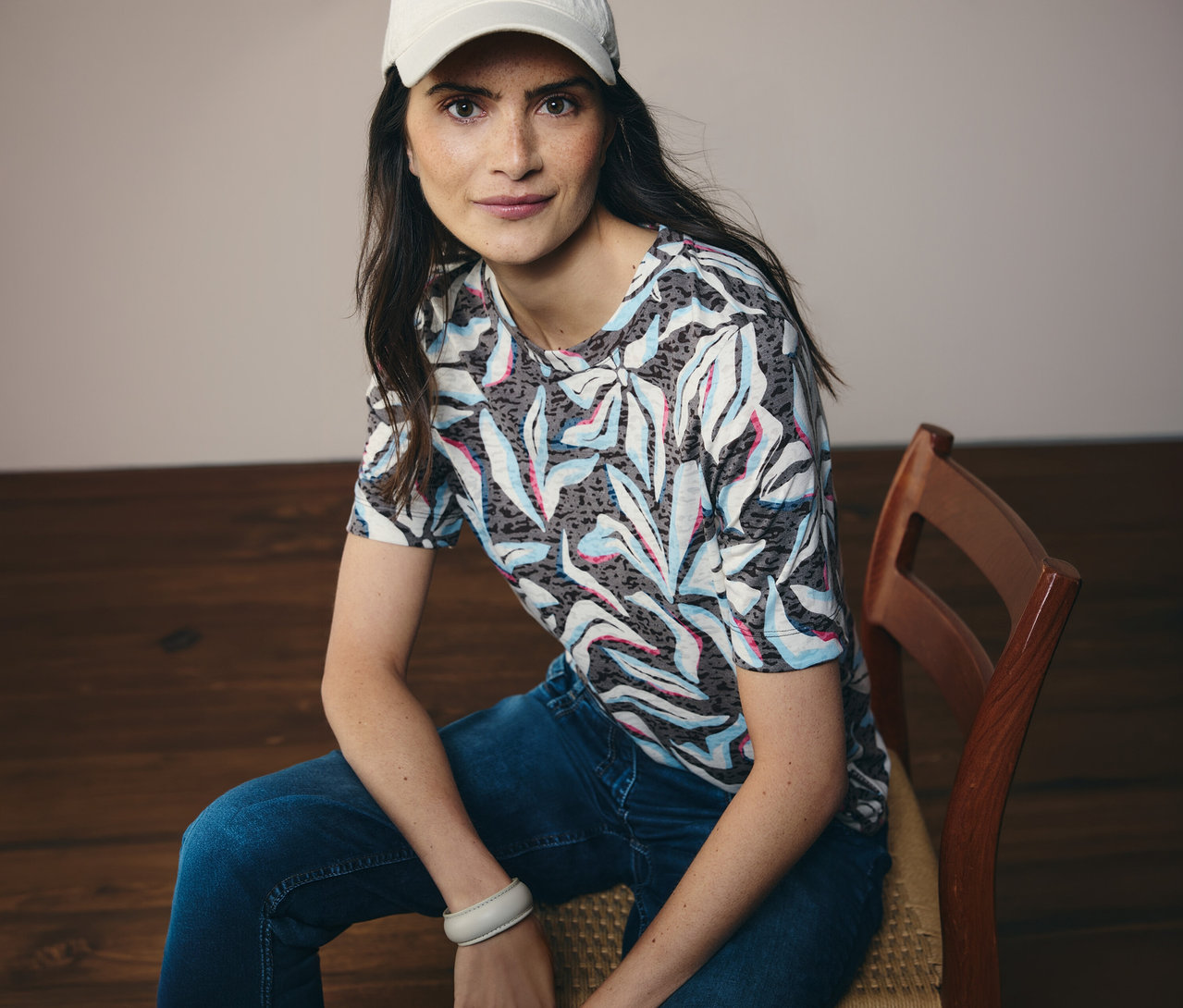 Kobieta w białej czapce siedzi i ma na sobie niebieską koszulkę z krótkim rękawem CECIL we wzory.