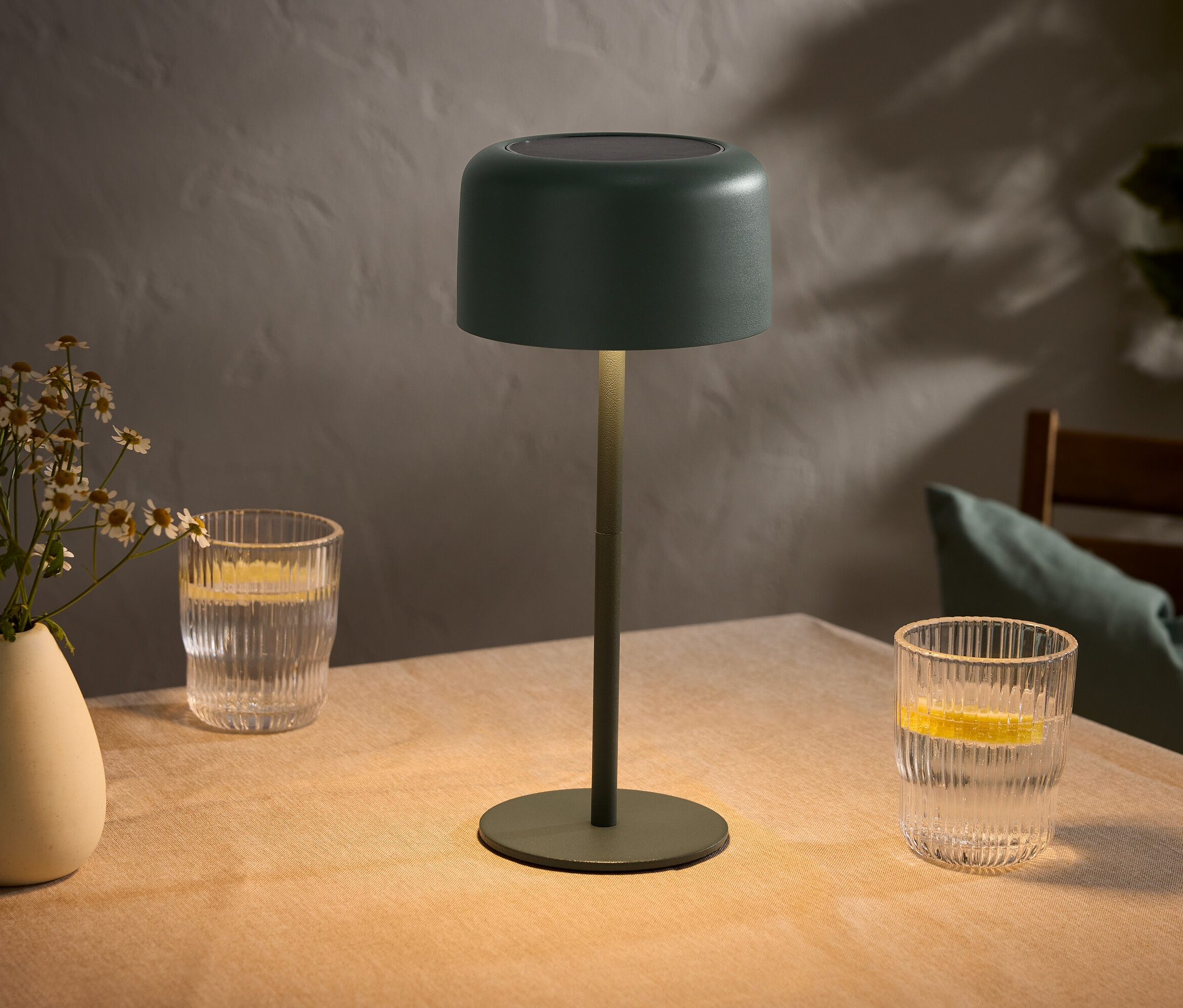 Stół z wazonem z kwiatami, dwiema szklankami z cytrynami i zieloną lampą.