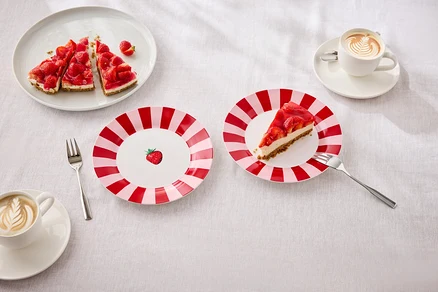Na stole leżą talerze z ciastem truskawkowym, widelce i filiżanki z latte art.