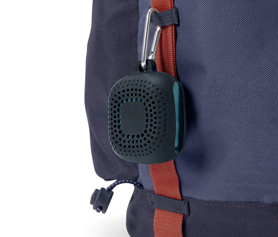 Czarny, okrągły futerał z otworami zwisa na karabińczyku z niebieskiego plecaka.