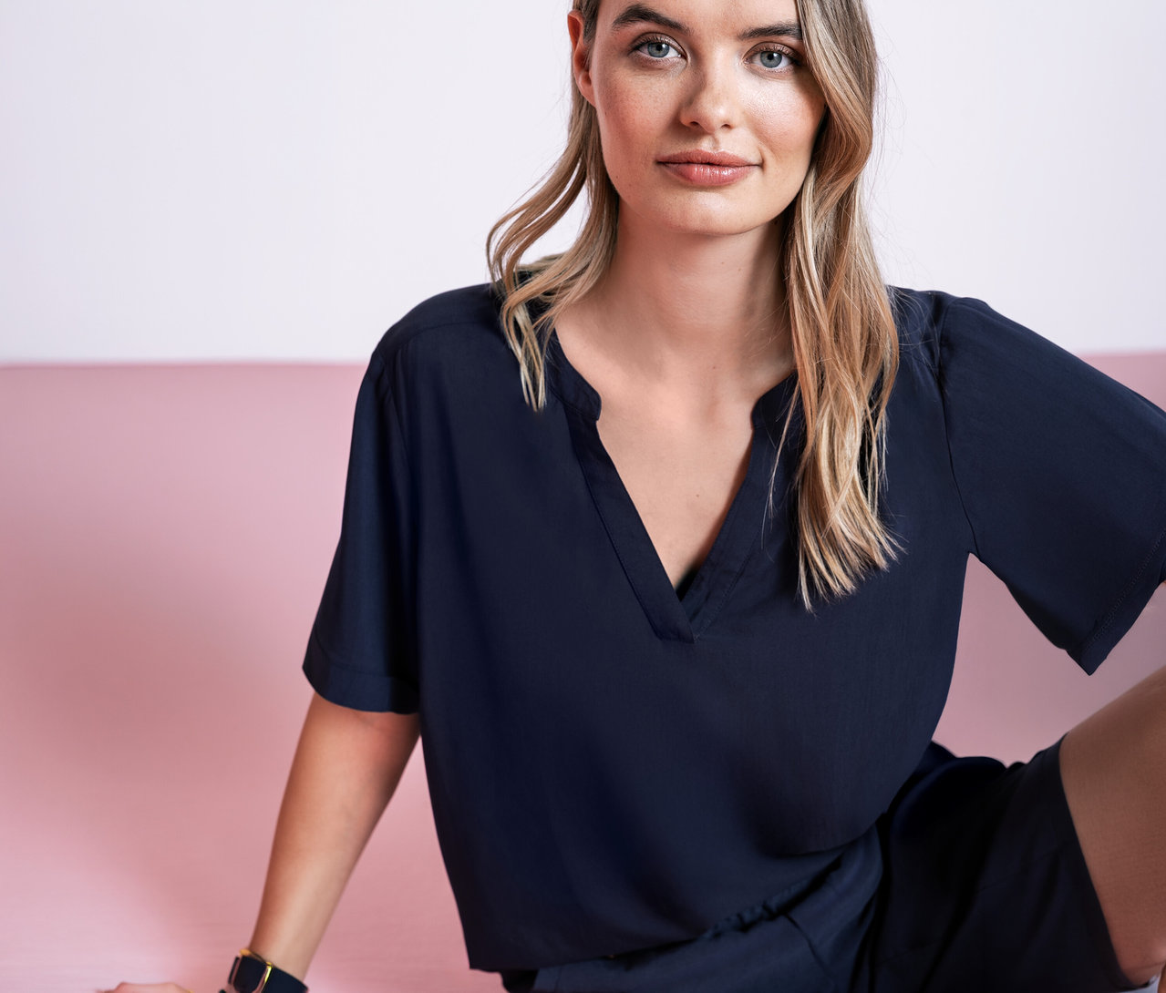 Kobieta siedzi na różowym tle, ubrana w granatową bluzkę z tkaniny Street One.