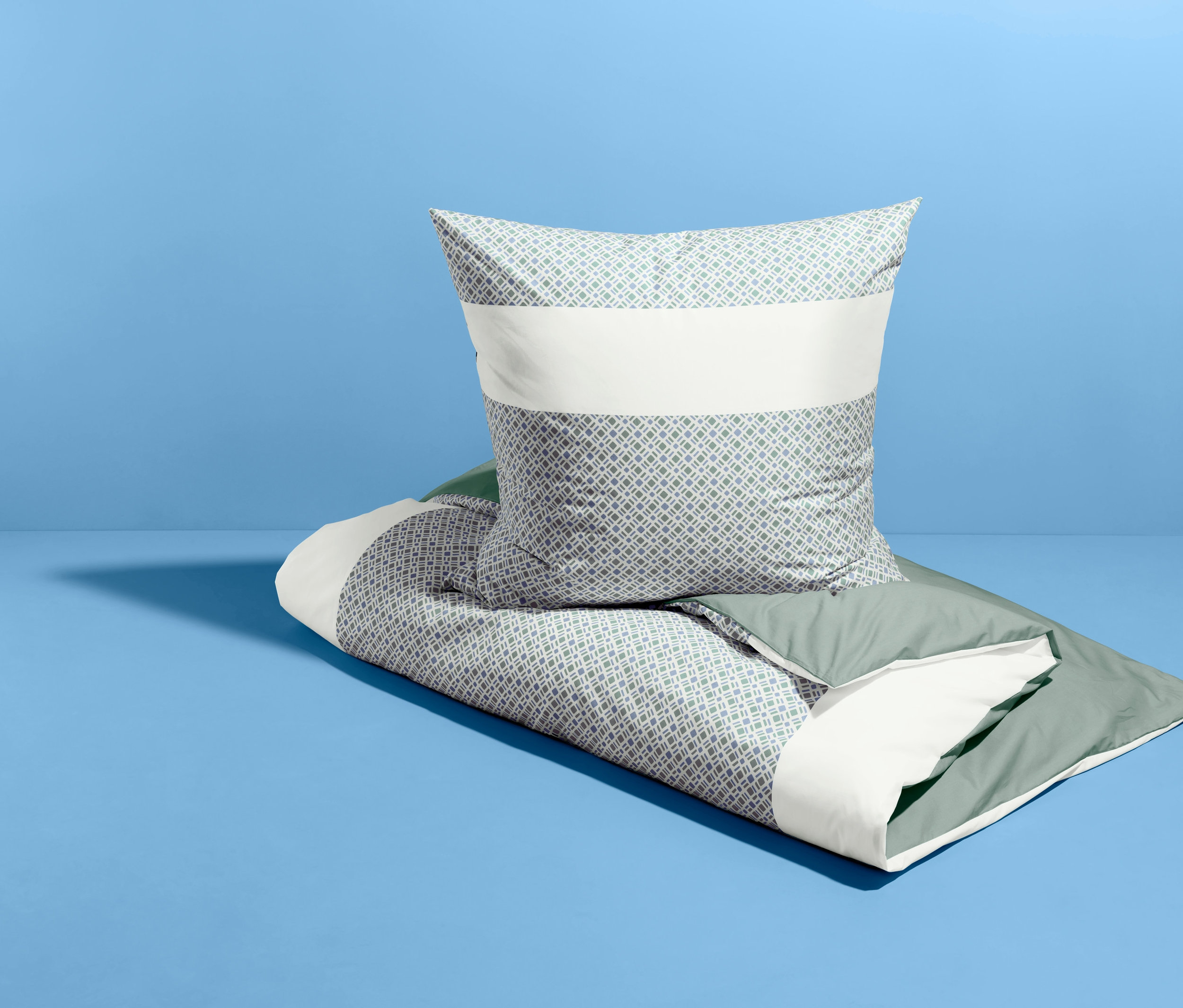Na niebieskim tle leży złożona pościel dwustronna z perkalu i poduszka.