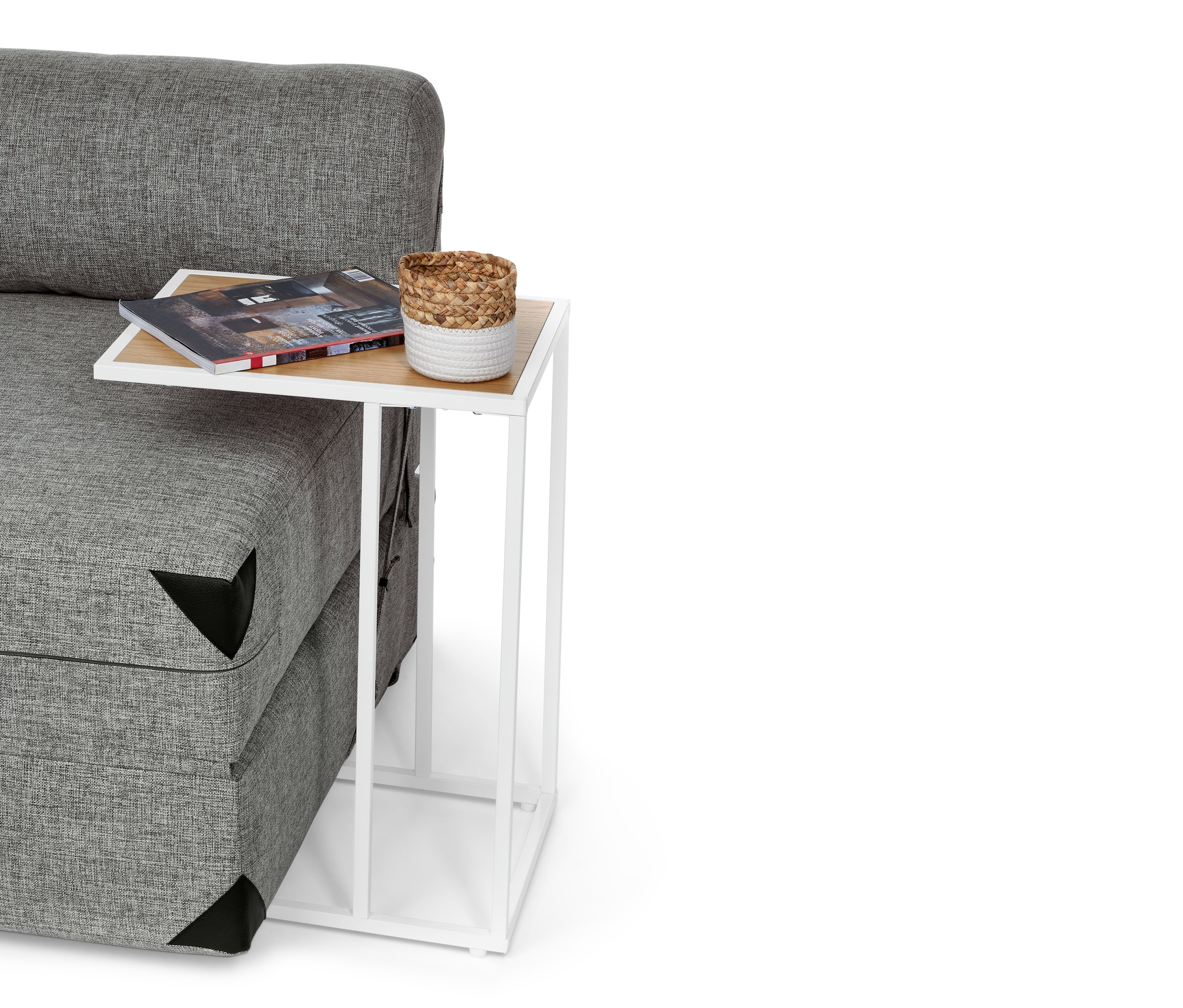 Szara sofa z białym stolikiem w kształcie litery C. Na stoliku leży magazyn i koszyk.