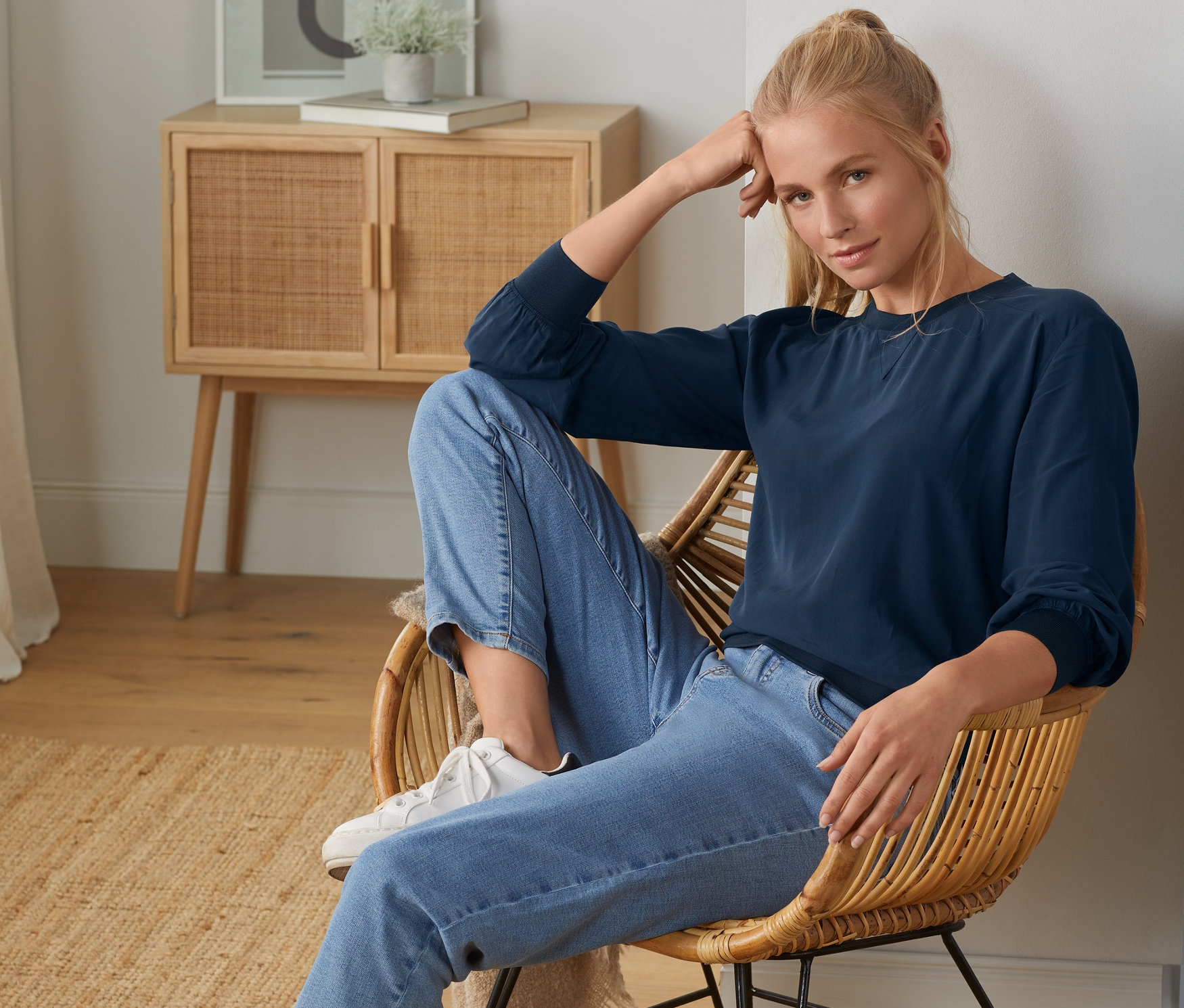 Blondynka siedzi na krześle i ma na sobie bluzkę ze ściągaczem.