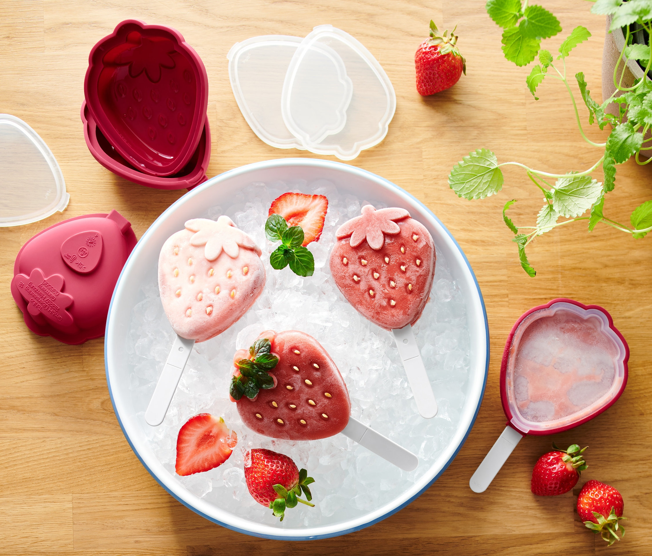 Trzy lody truskawkowe na patyku na lodzie w misce obok Foremki do lodów, 4 sztuki.