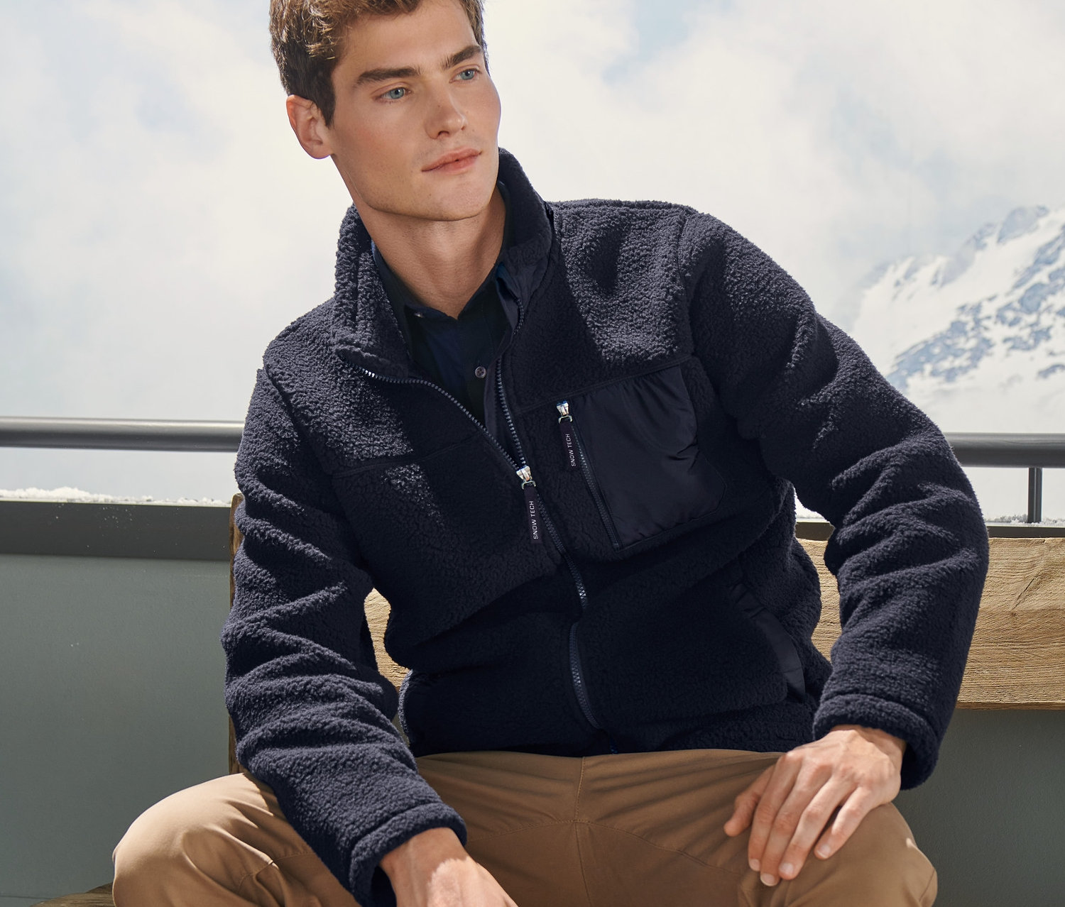 Mężczyzna siedzi na ławce, ubrany w kurtkę z puszystego pluszu.