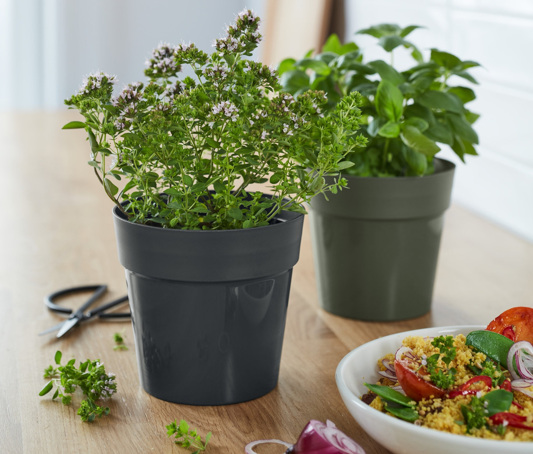 Dwie ozdobne doniczki na zioła stoją na drewnianym blacie obok sałatki.