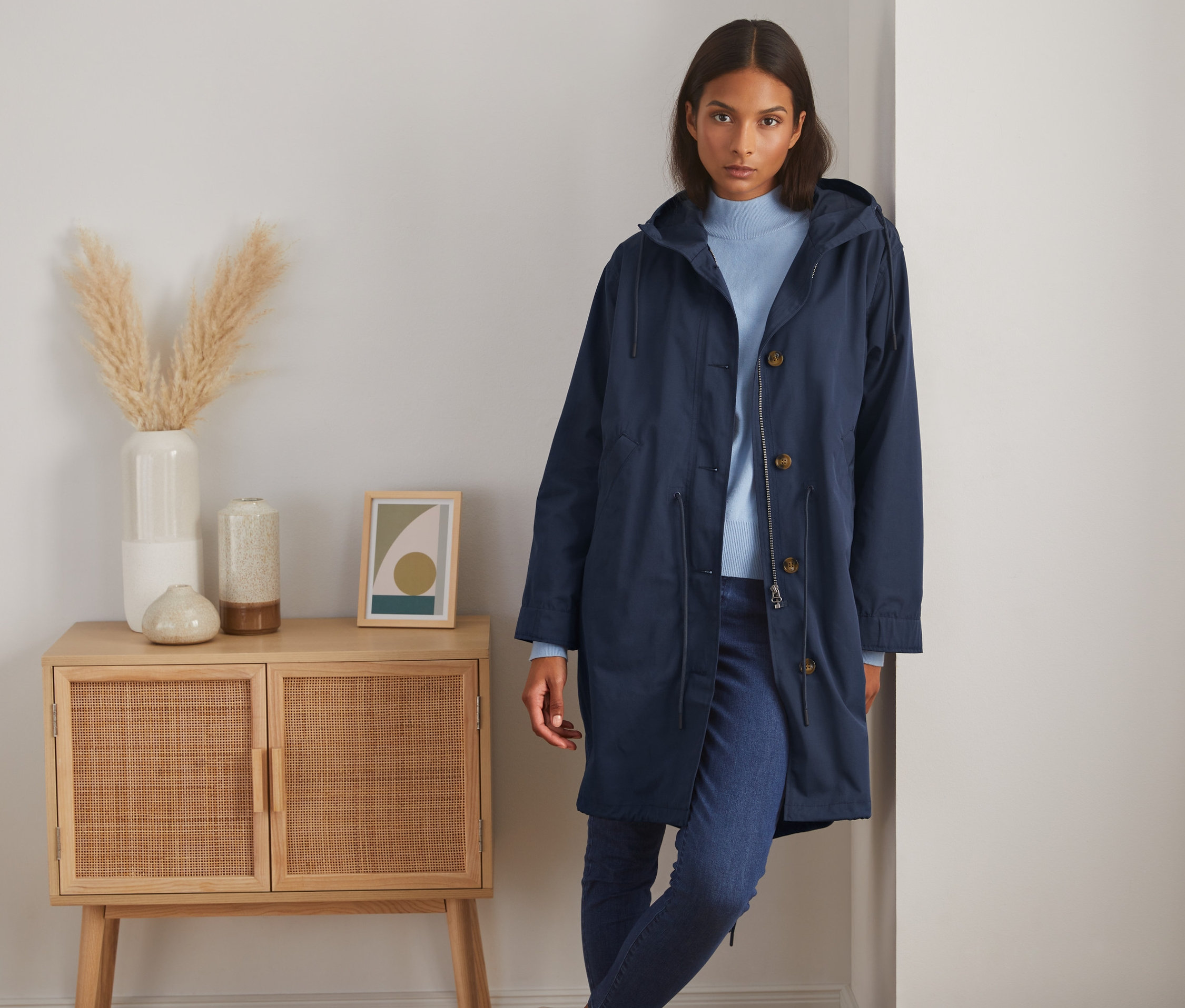 Kobieta pozuje w granatowej parce z kapturem obok szafki.