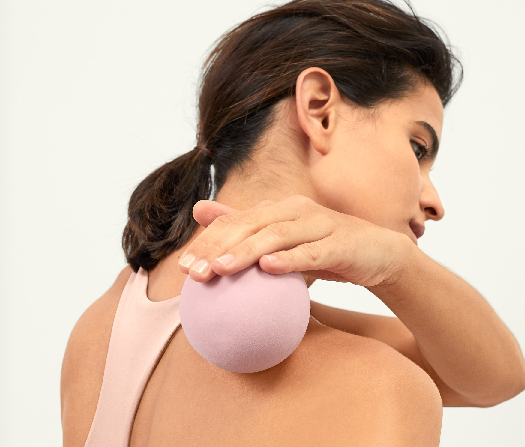 Kobieta masuje górną część pleców piłeczką do masażu powięzi.