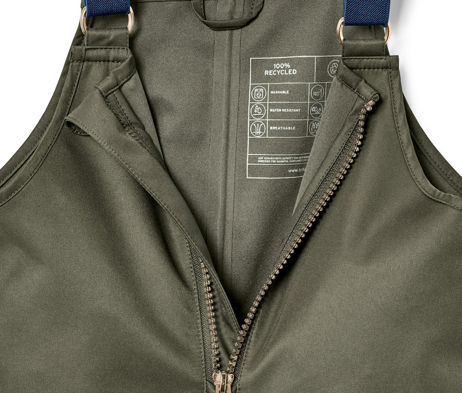 Zbliżenie na oliwkowozielone spodnie przeciwdeszczowe z rozpiętym zamkiem błyskawicznym i niebieskimi szelkami.