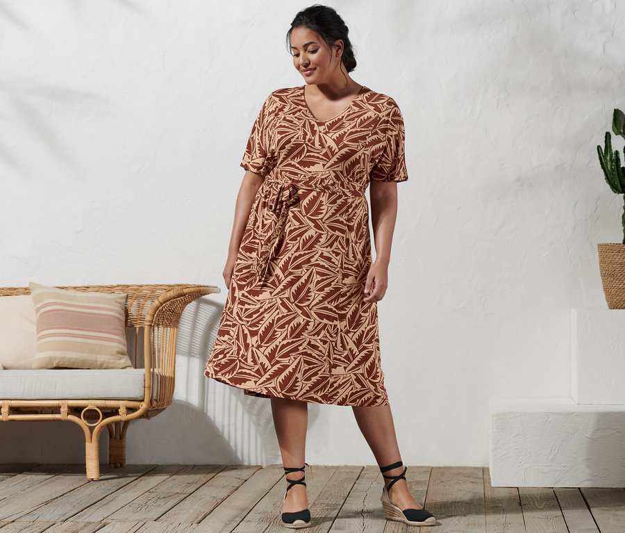 Kobieta stoi i ma na sobie sukienkę dżersejową z nadrukiem i espadryle na koturnie.