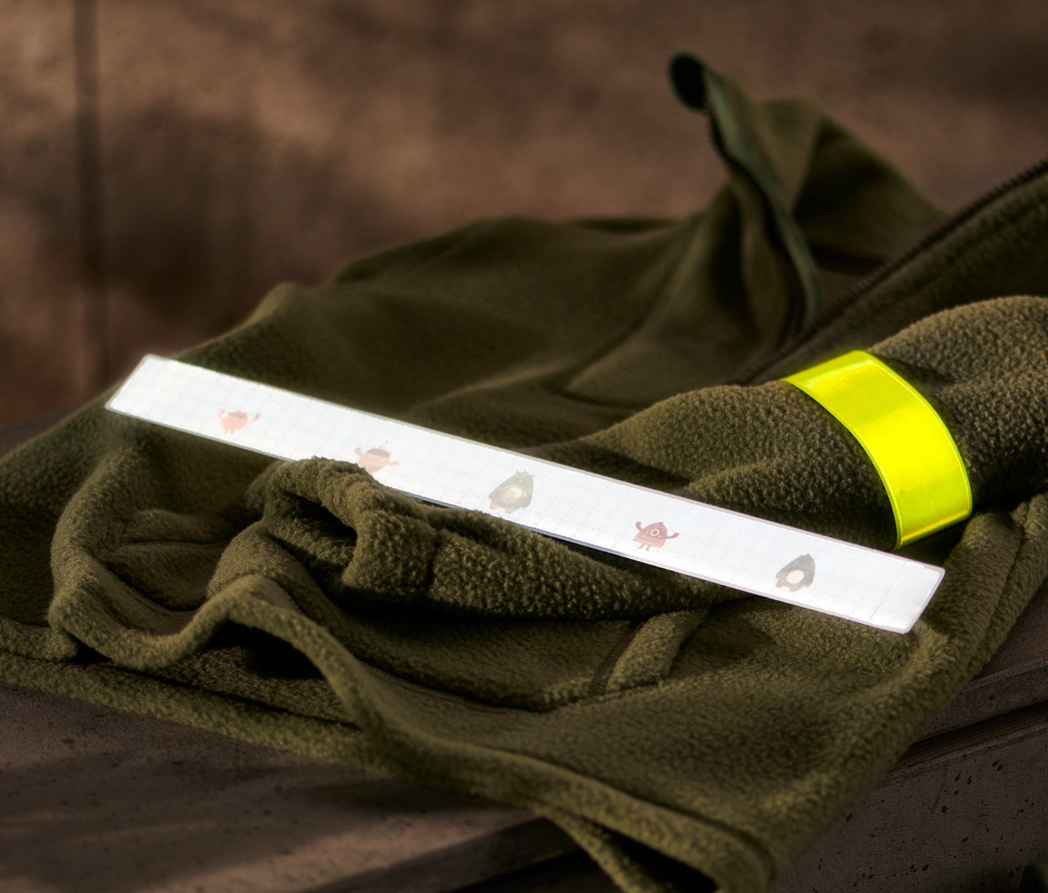Na oliwkowozielonej bluzie polarowej leżą odblaskowe opaski samozaciskowe, 2 sztuki.