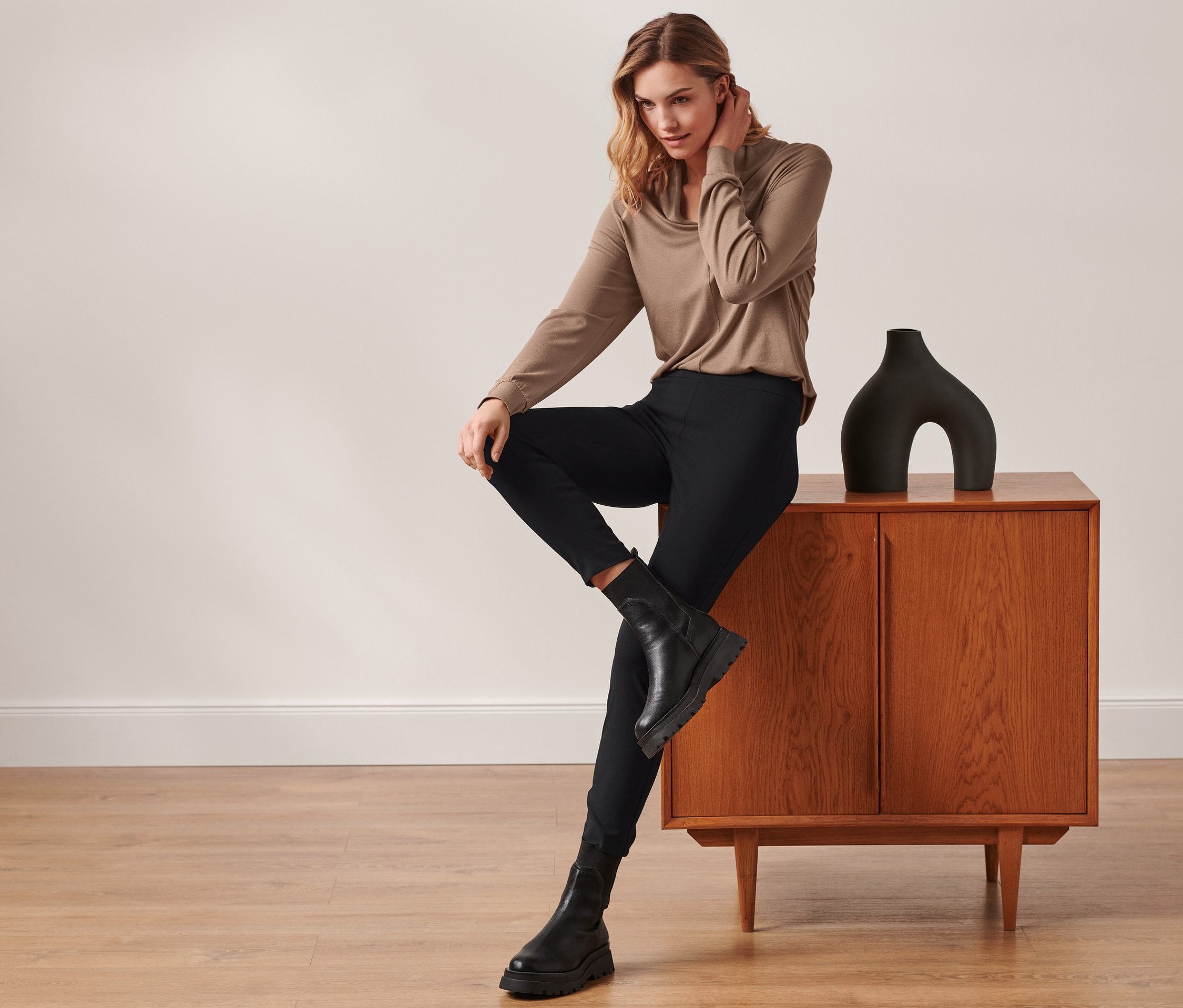 Kobieta siedzi na szafce, ubrana w czarne spodnie stretchowe.