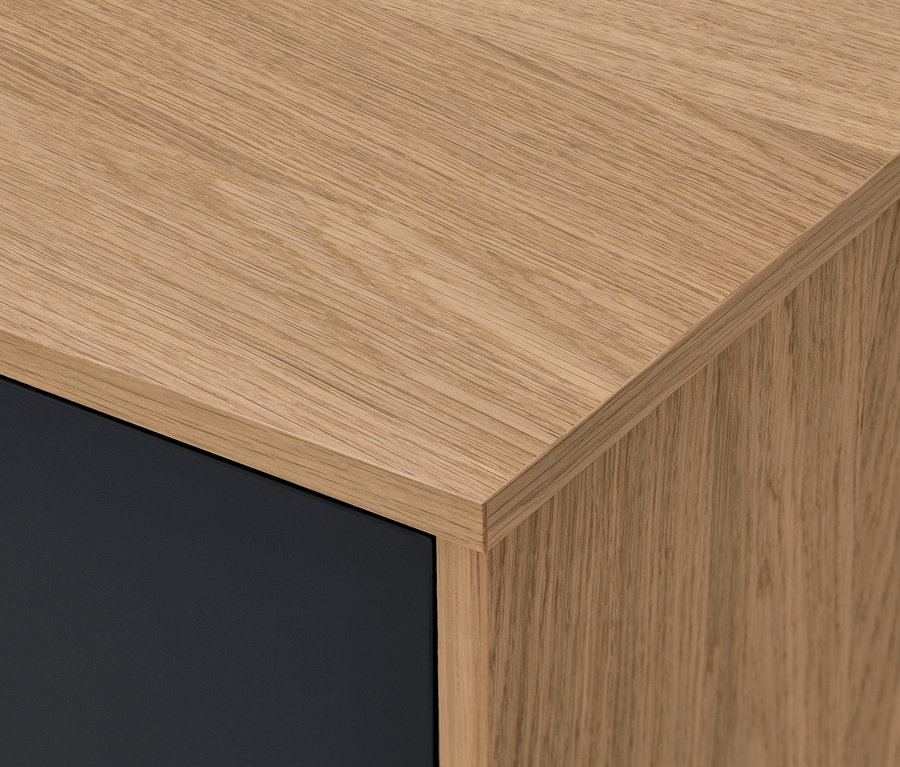 Detal narożnika komody Bekeson w kolorze antracytowym z drewnianym blatem.