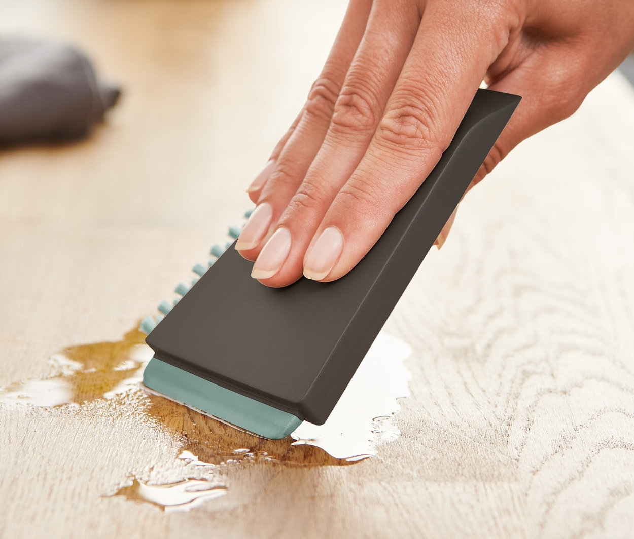 Kobieta wyciera płyn z drewnianej powierzchni uniwersalną szczotką kuchenną.