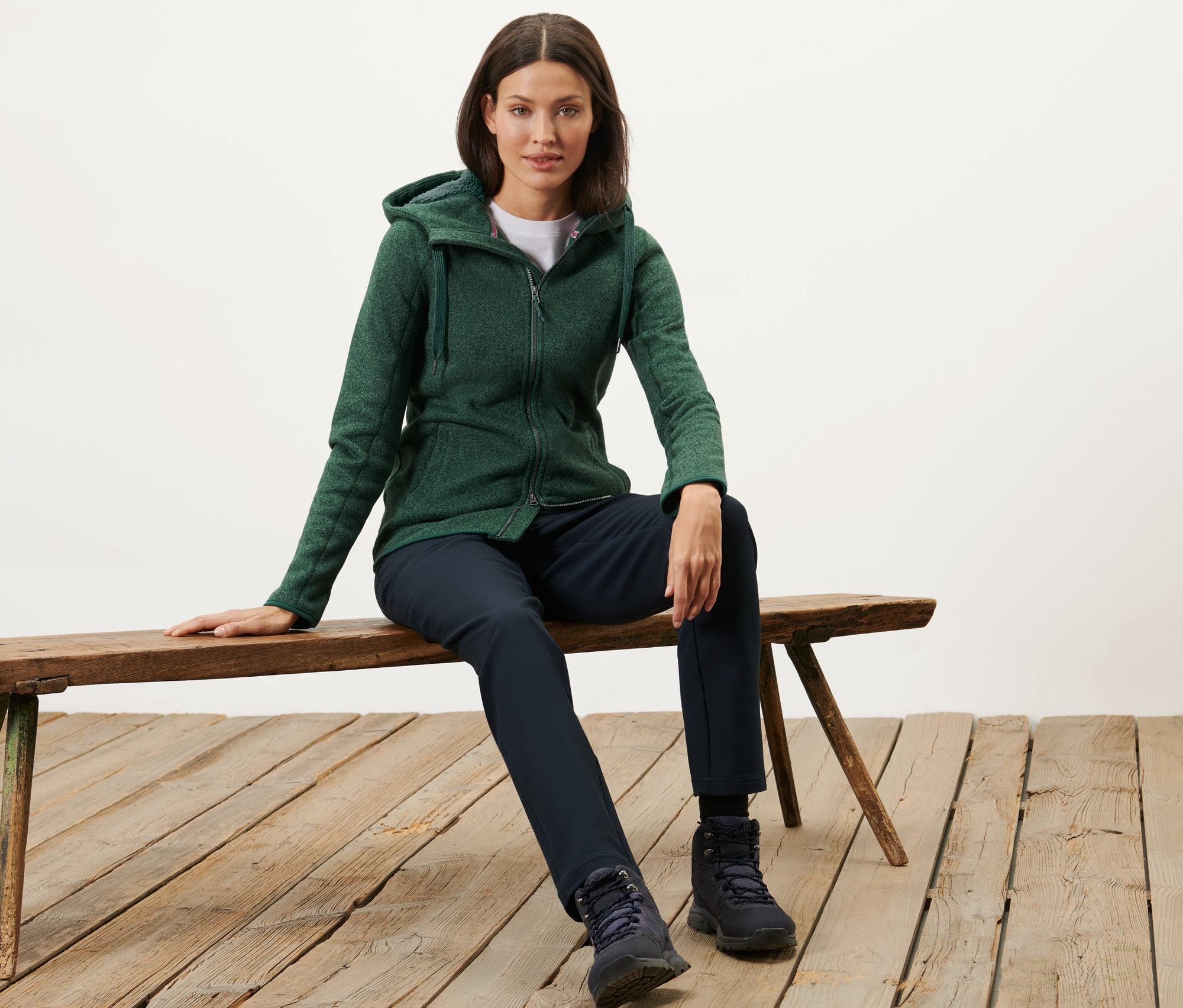 Kobieta siedzi na ławce, ubrana w zieloną bluzę z kapturem z dzianiny polarowej, zielony melanż.
