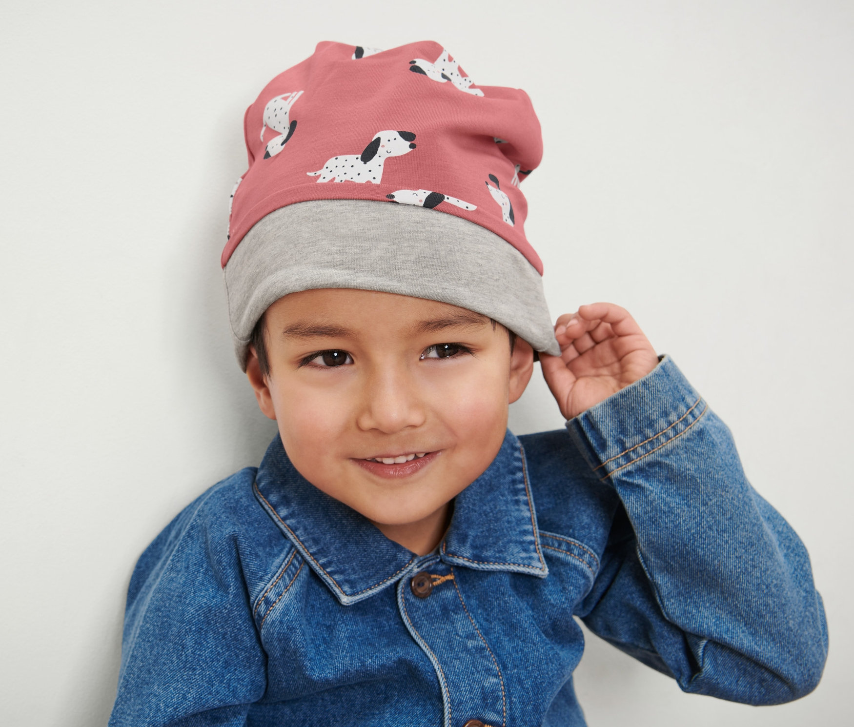 Chłopiec ma na sobie różowo-szarą czapkę dziecięcą i kurtkę dżinsową.