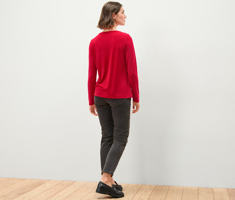 Kobieta stoi tyłem, ma na sobie bluzkę z marszczeniem, dżinsy i buty.