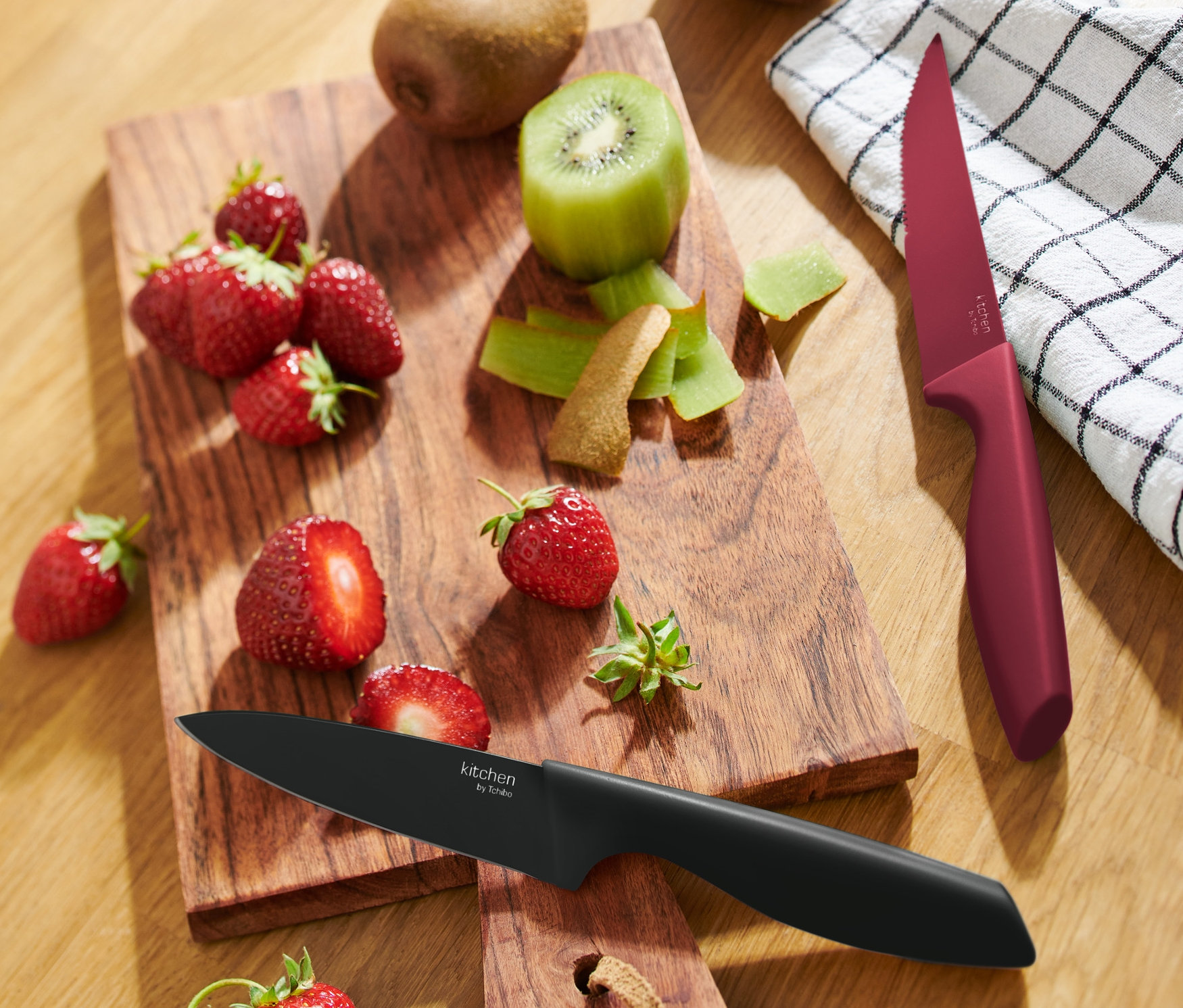 Truskawki i kiwi na drewnianej desce do krojenia z dwoma nożami kuchennymi.