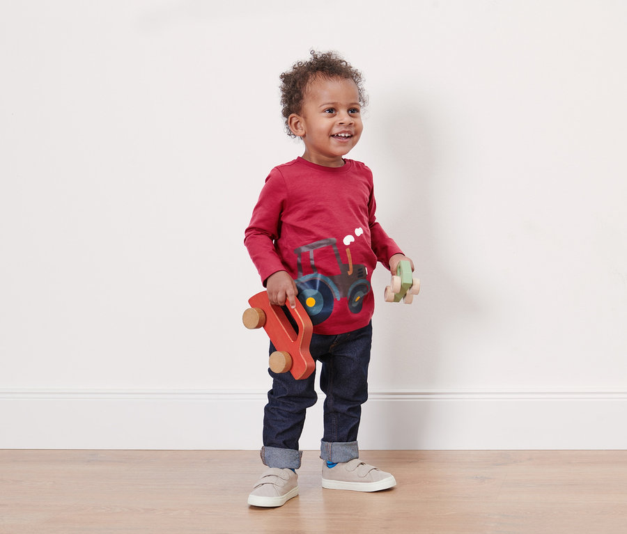 Chłopiec w czerwonej koszulce z traktorem trzyma dwa drewniane autka.