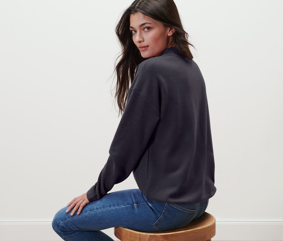 Kobieta siedzi na stołku, ubrana w bluzę ze stójką.