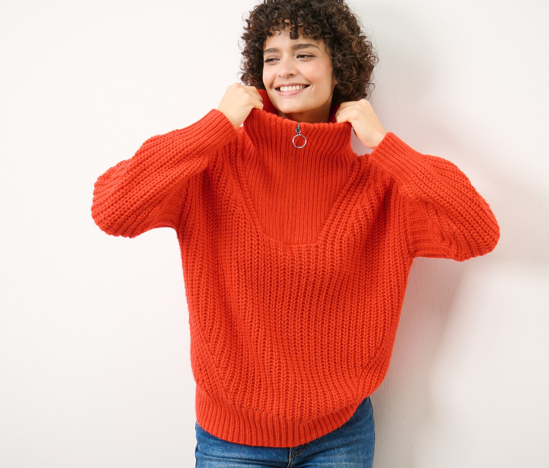 Kobieta podciąga kołnierz pomarańczowego grubego golfu z rozpinanym kołnierzem do szyi.