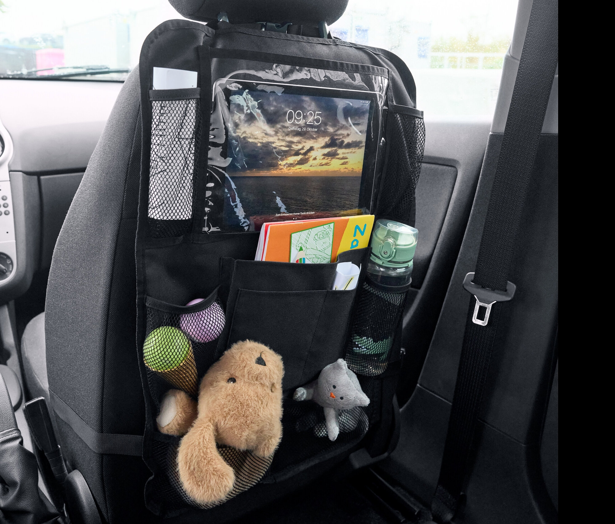 Czarny organizer na oparcie fotela z zabawkami, książkami i tabletem.