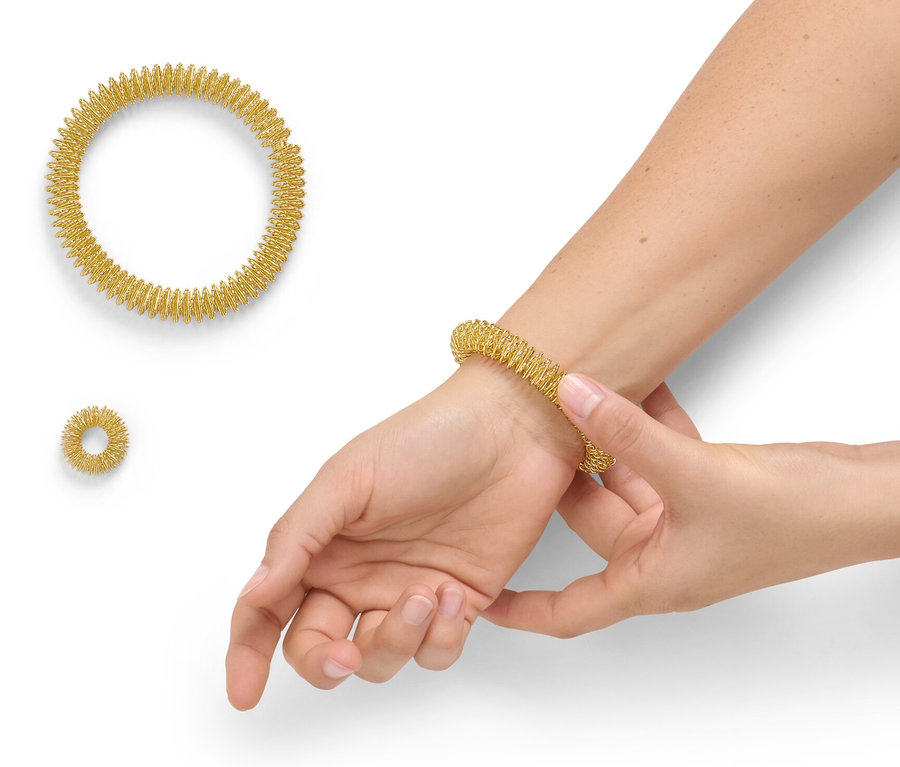 Kobieta zakłada złoty pierścień do akupresury z zestawu do akupresury na nadgarstek. Obok leżą dwa inne pierścienie.