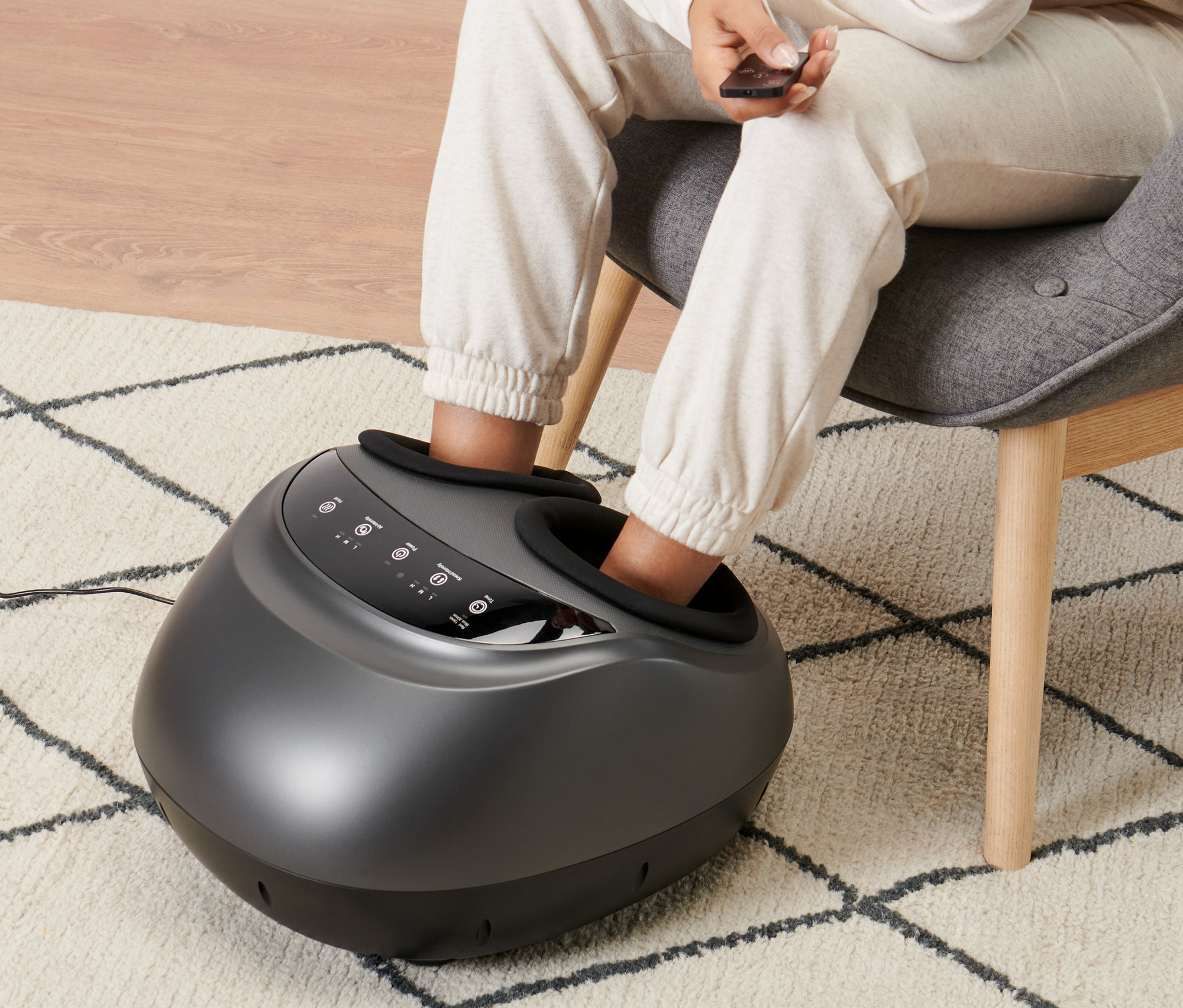 Kobieta siedzi w fotelu i używa urządzenia do masażu stóp.