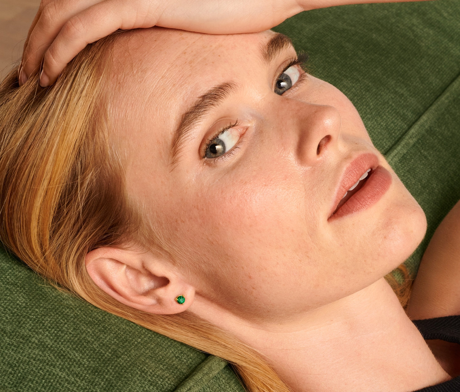 Blondwłosa kobieta leży na zielonej sofie i ma na sobie kolczyki na sztyft zestaw.