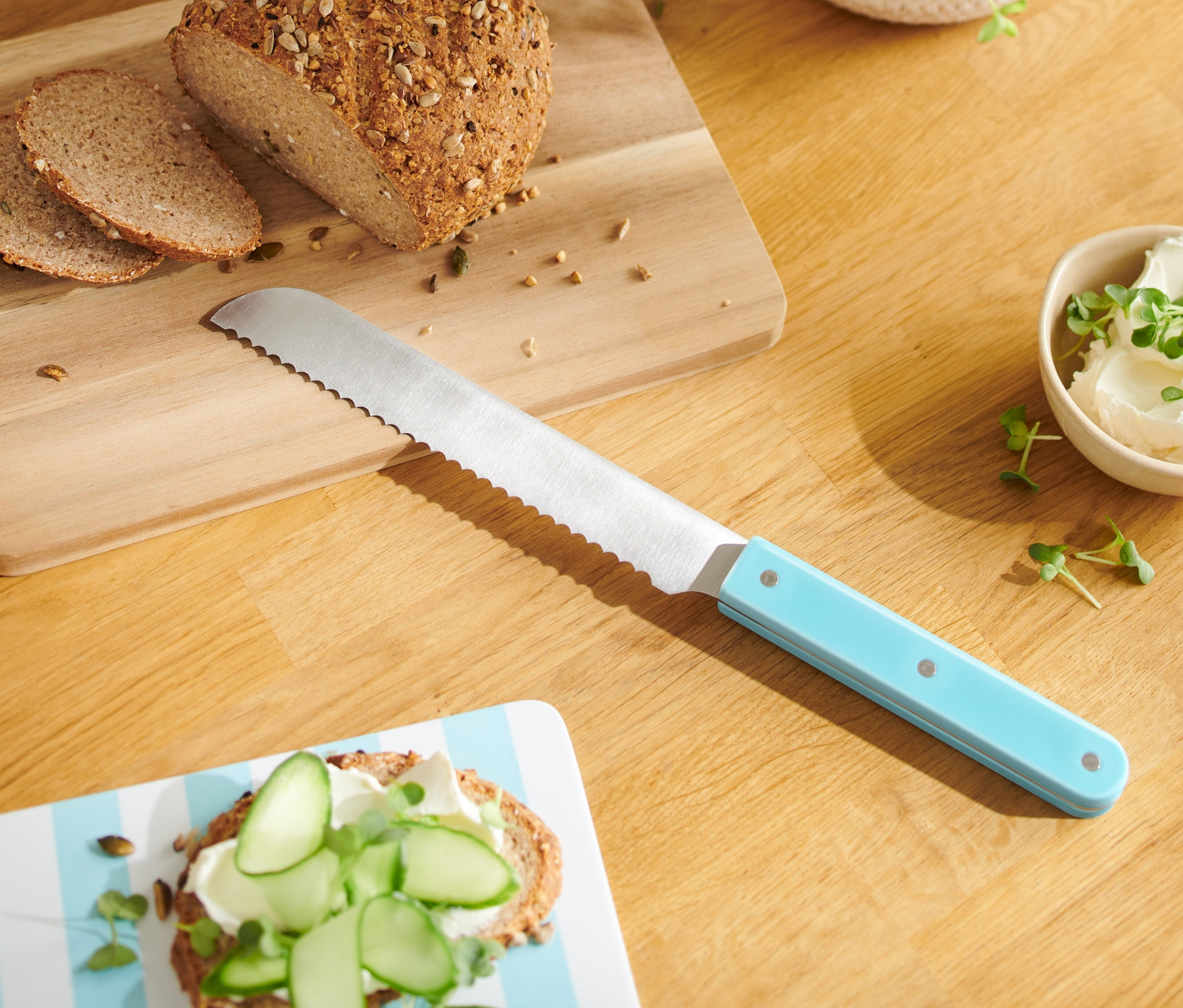 Chleb i dwie kromki na drewnianej desce z nożem kuchennym z niebieską rączką.