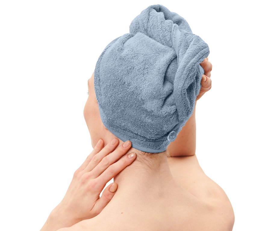 Kobieta z jasnoniebieskim ręcznikiem turbanem na głowie i ręcznikiem w tym samym kolorze owiniętym wokół ciała.