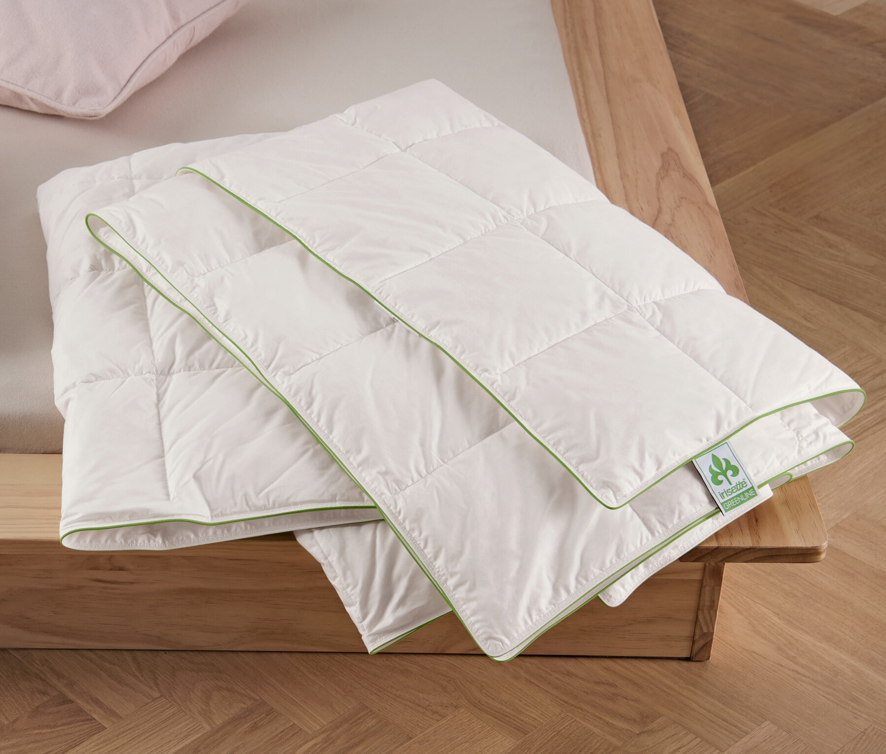 Dwie poduszki i złożona letnia kołdra puchowa irisette® greenline w rozmiarze standardowym na łóżku.