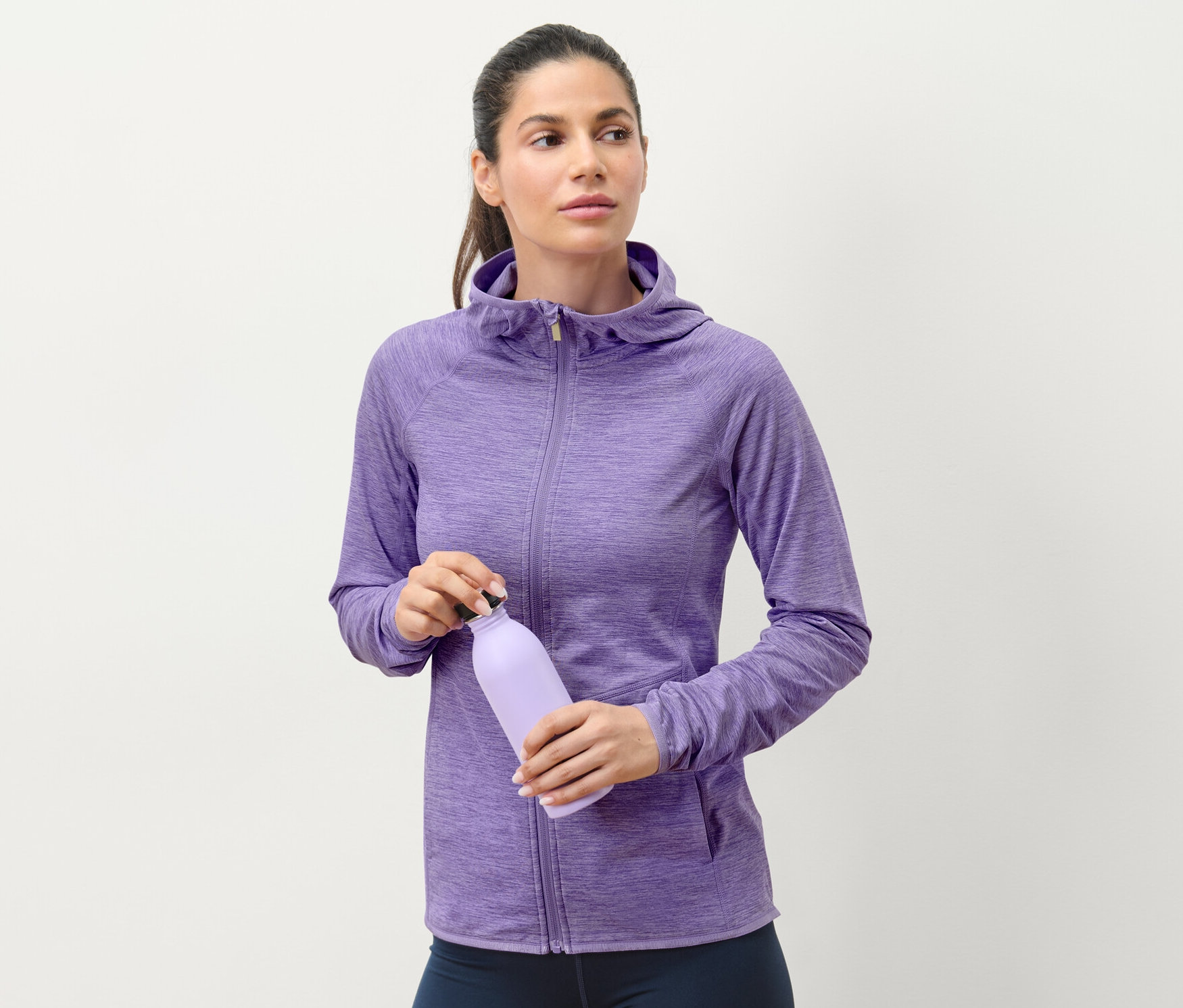 Kobieta trzyma fioletową butelkę z wodą i ma na sobie bluzę sportową w liliowy melanż.