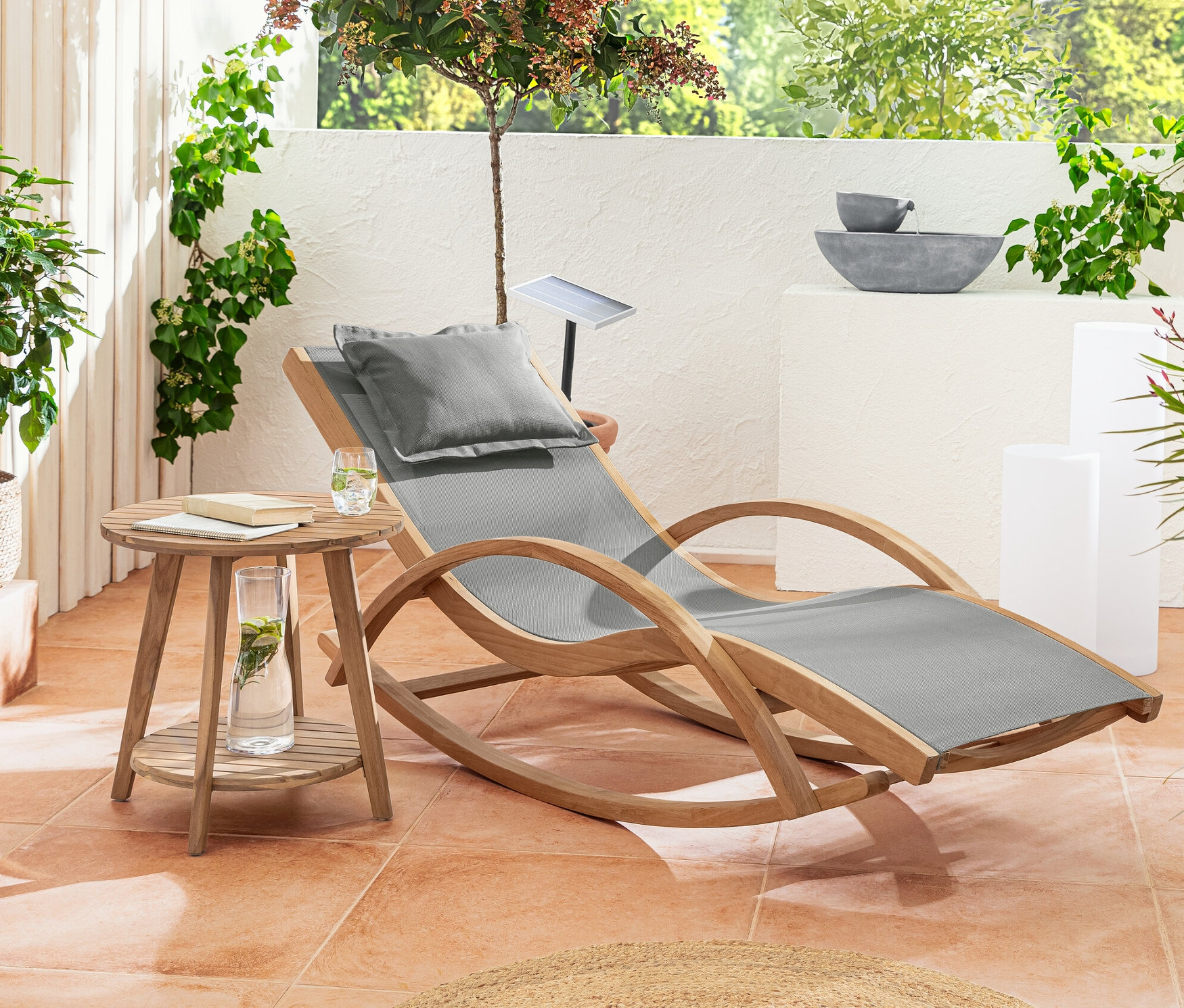 Na tarasie stoją leżak bujany z drewna tekowego, stolik dwupoziomowy „Lenja” i solarny słupek świetlny z przepływem kolorów, ok. 50 cm.