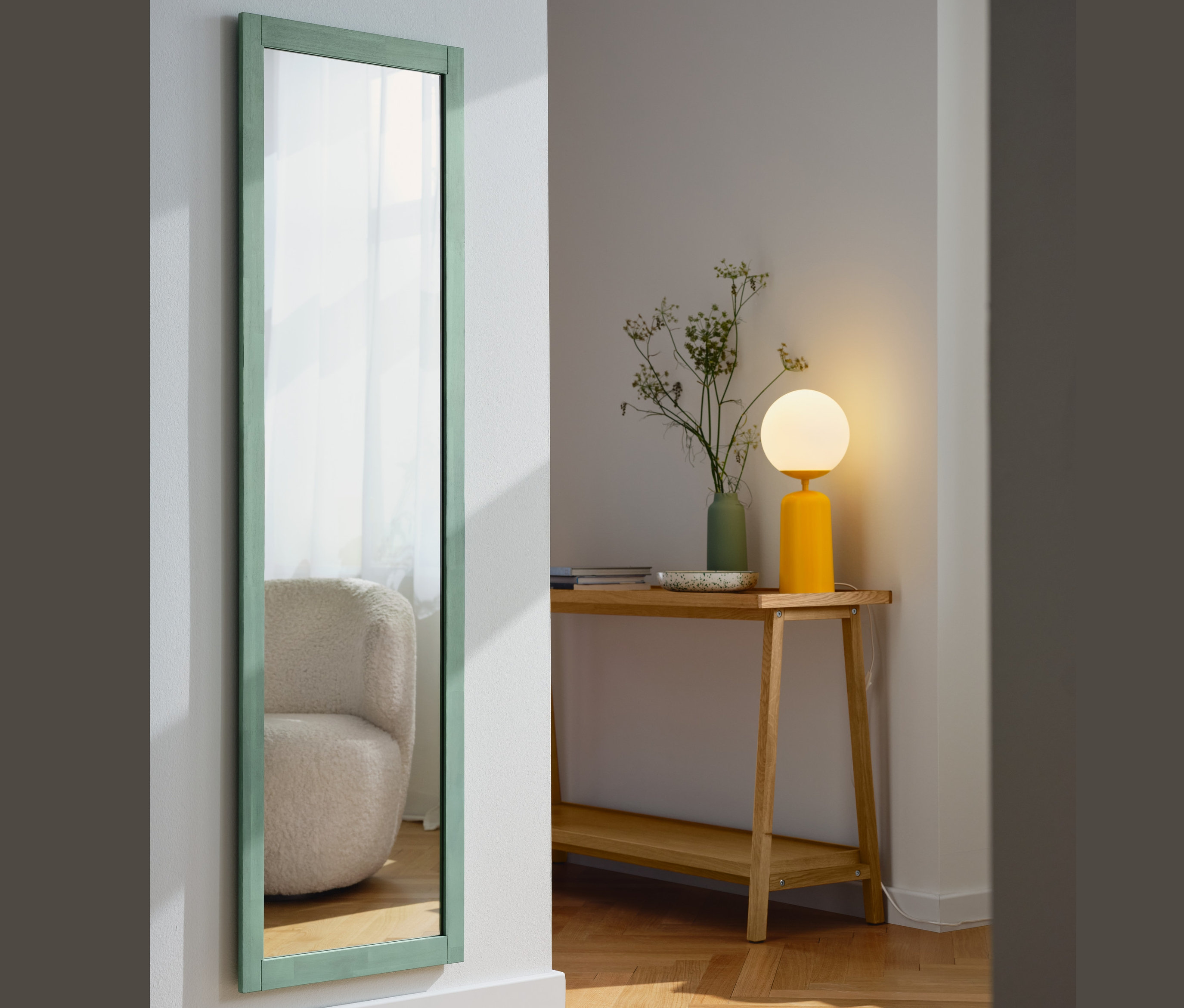 W przedpokoju stoi konsola z 2 półkami, na której znajduje się żółta lampa stołowa ze szklaną kulą. Obok stoi wysokie lustro w ramie, szałwiowa zieleń.