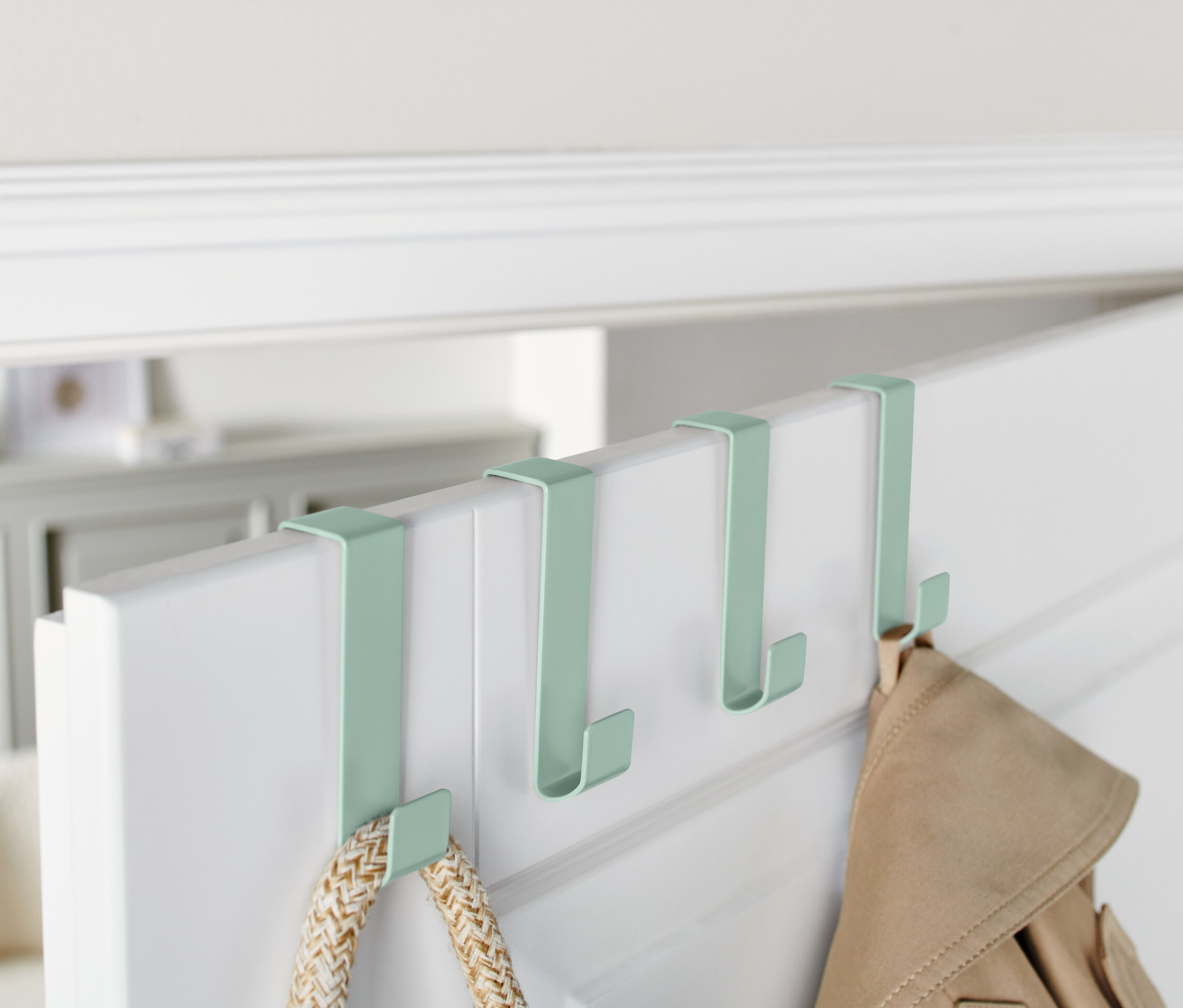 Cztery zielone haczyki na drzwi wiszą na górnej krawędzi białych drzwi.